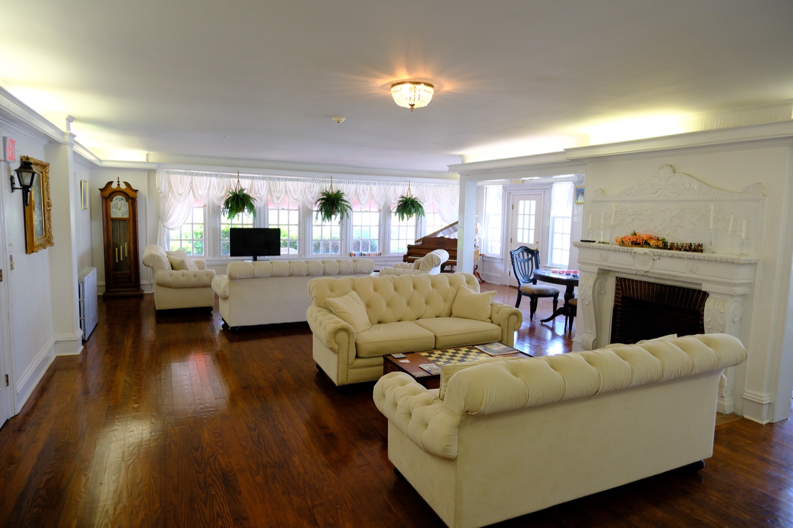 The grand living room of the Plymouth Inn with tufted cream sofas, a carved fireplace, grandfather clock and baby grand piano