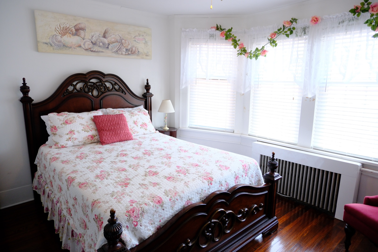 Queen Mum's Suite 3 with a carved wood bed in rose floral linens beneath seashell artwork